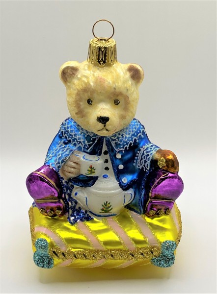 Bär sitzt im blauen Prinzenkostüm auf einem Kissen und trinkt Tee, KOMOZJA MOSTOWSKI