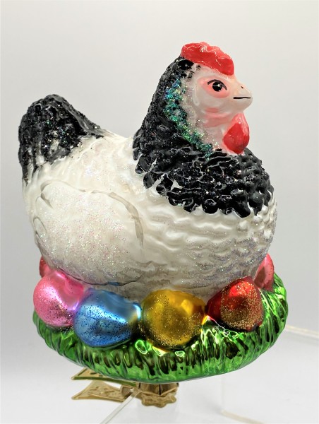 Schwarzweisses Huhn sitzt auf den bunten Eiern im Nest